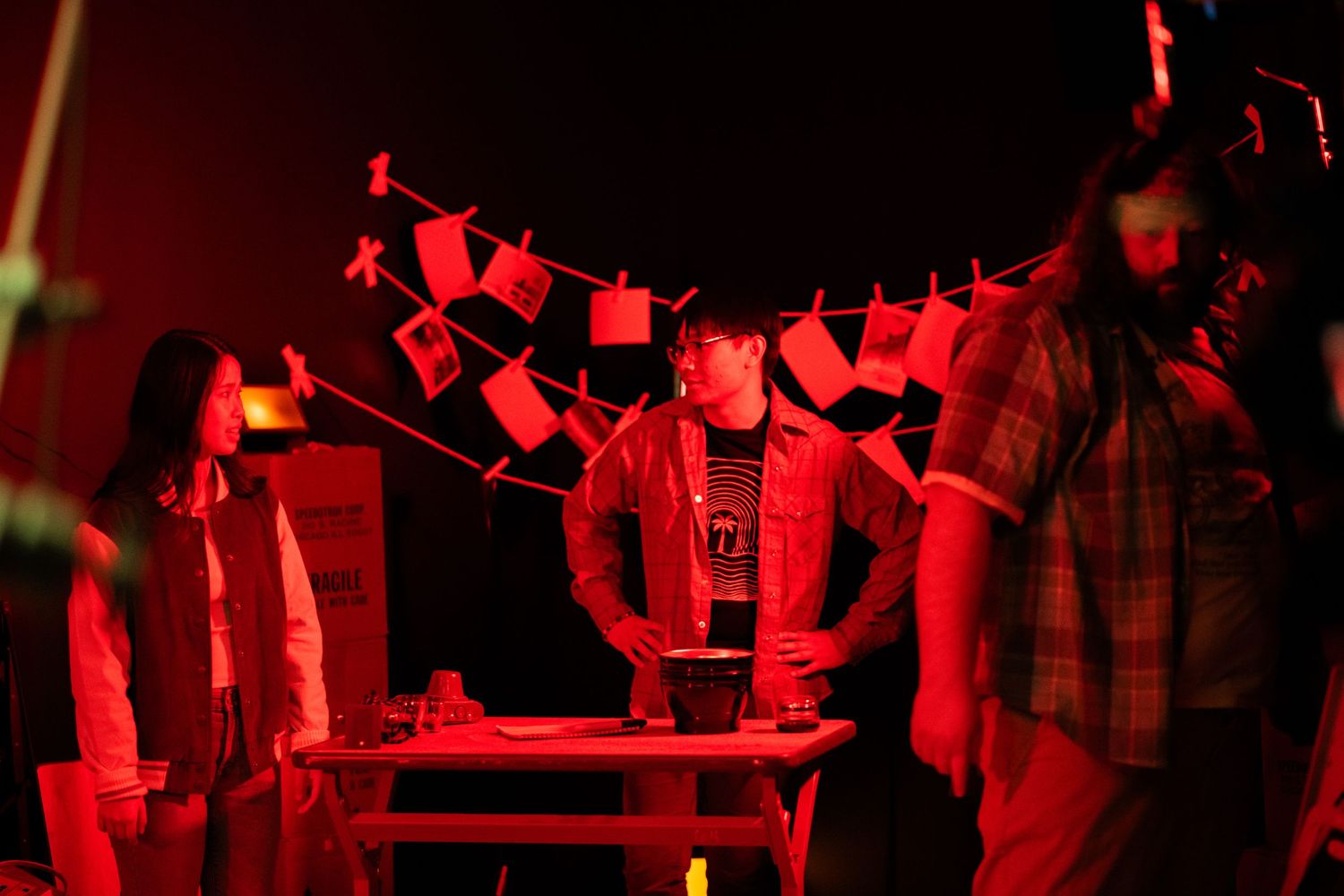 Film crew members gathered around a table on a red-lit movie production set.