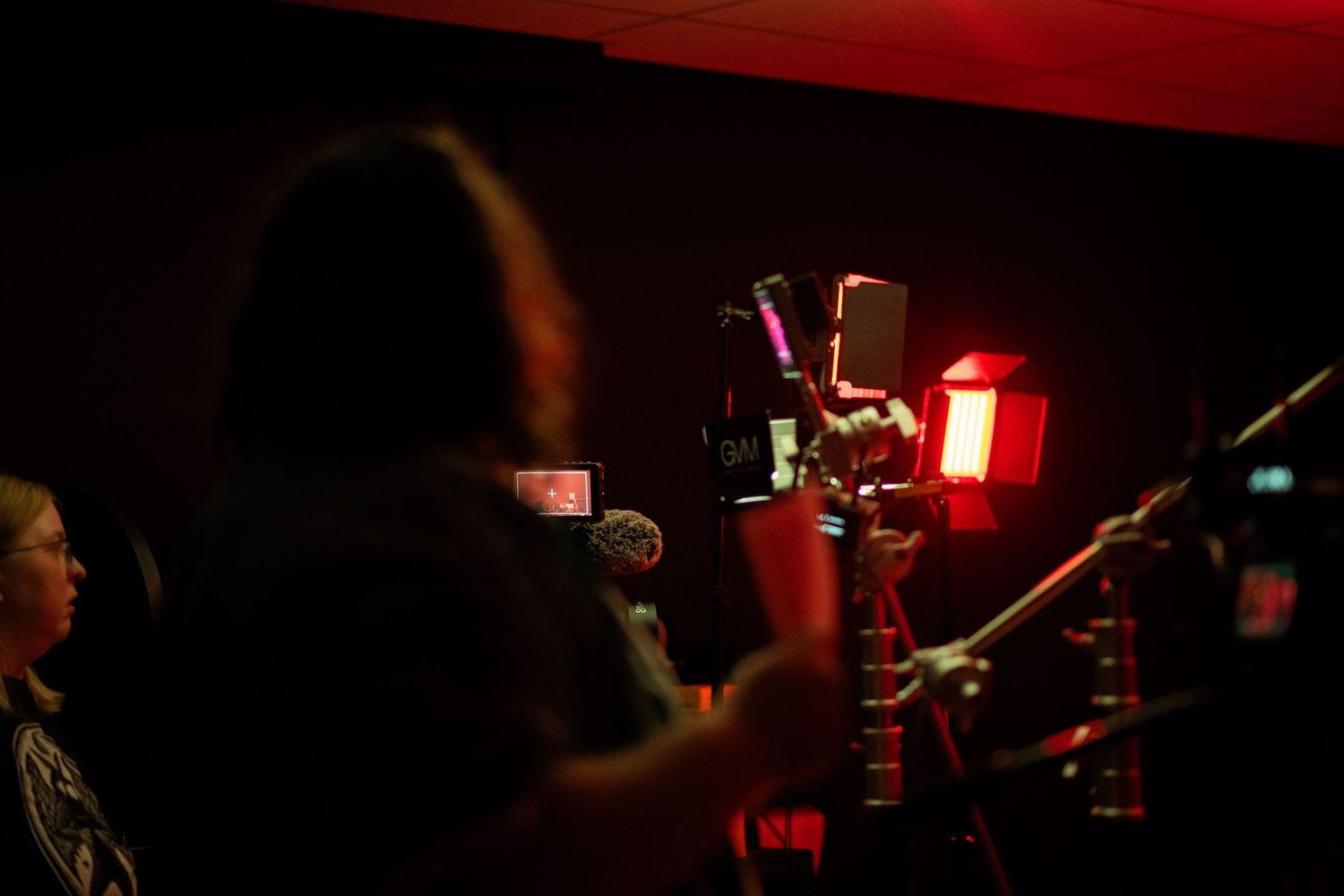 A camera operator films a live event in a dark venue illuminated by dramatic red lighting.