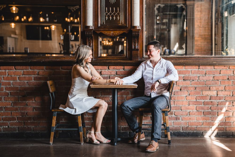 Two people share drinks at a rustic bar with exposed brick walls and warm lighting.