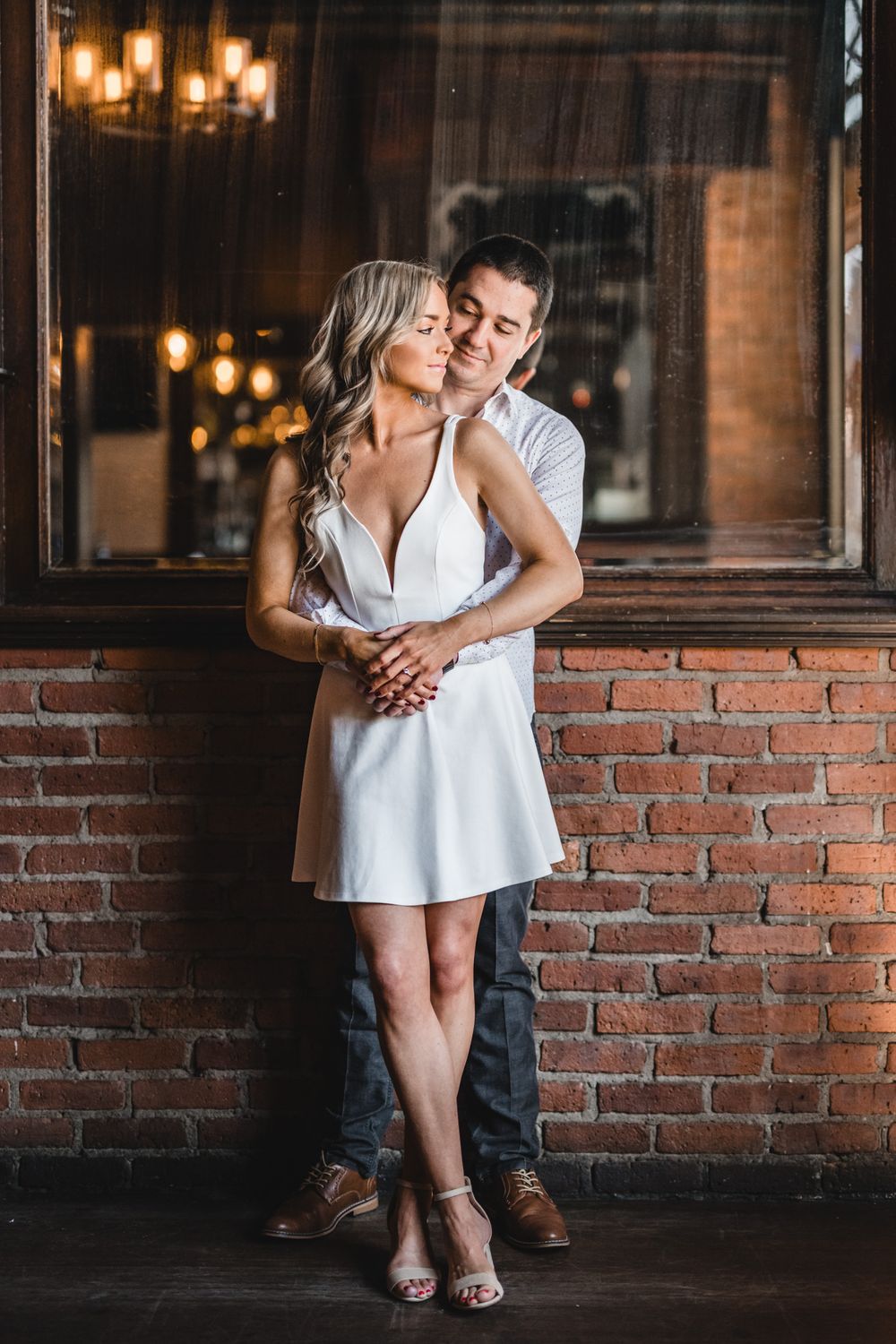 Romantic embrace against brick wall with warm bar lighting in background.