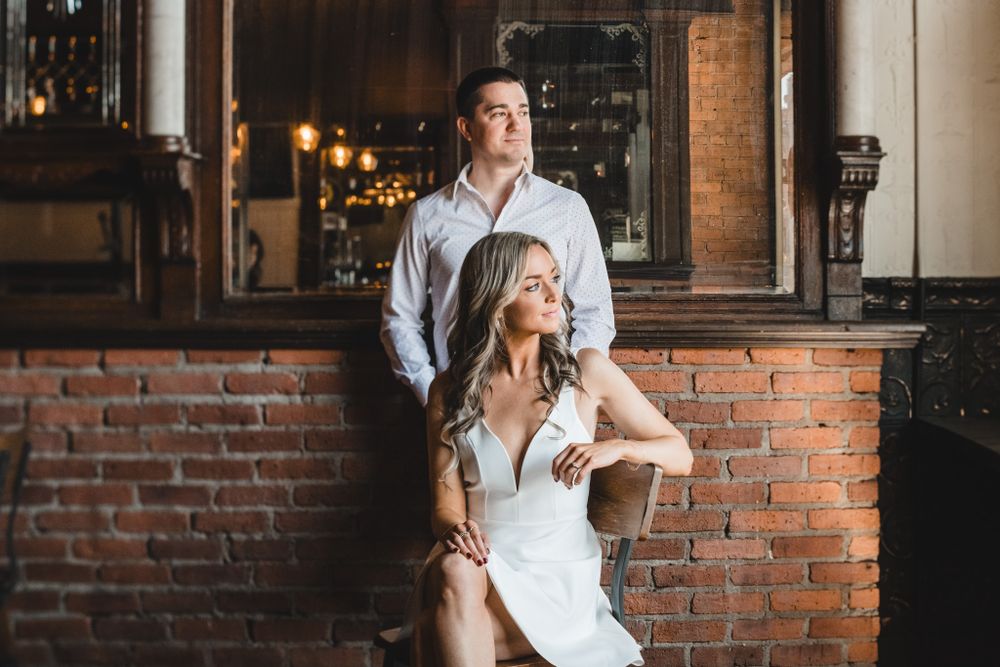 Couple embracing in front of rustic brick wall interior.