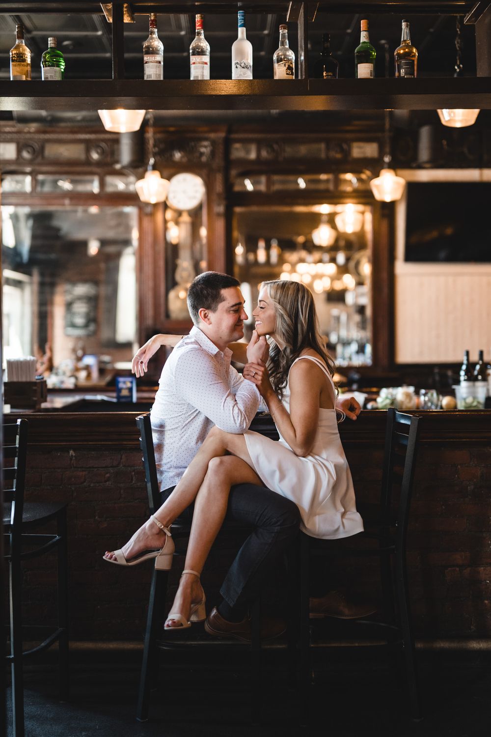 Couple sharing romantic moment at bar with bottles displayed in background.