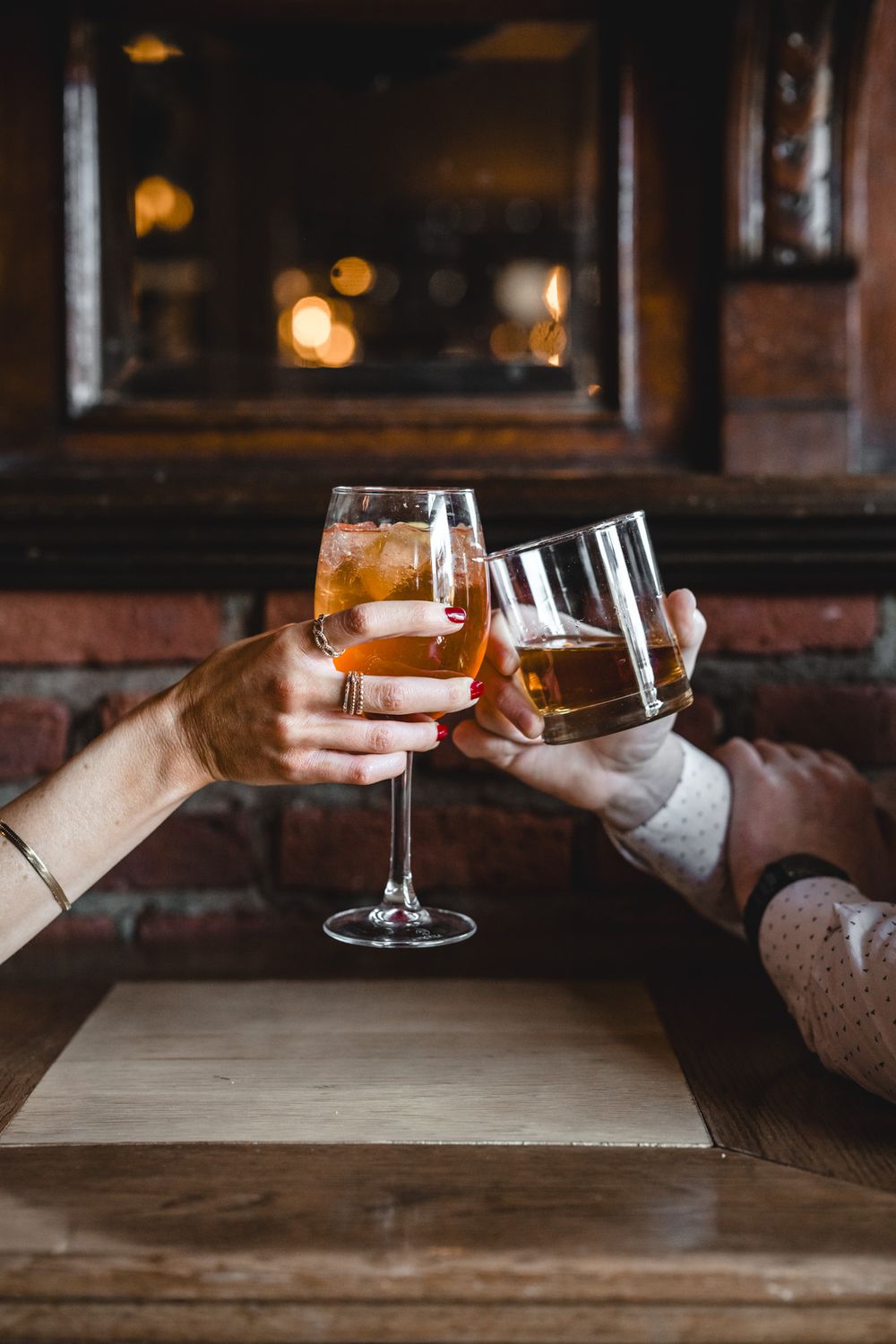 Two hands toasting with wine glasses in front of a dark wooden table.