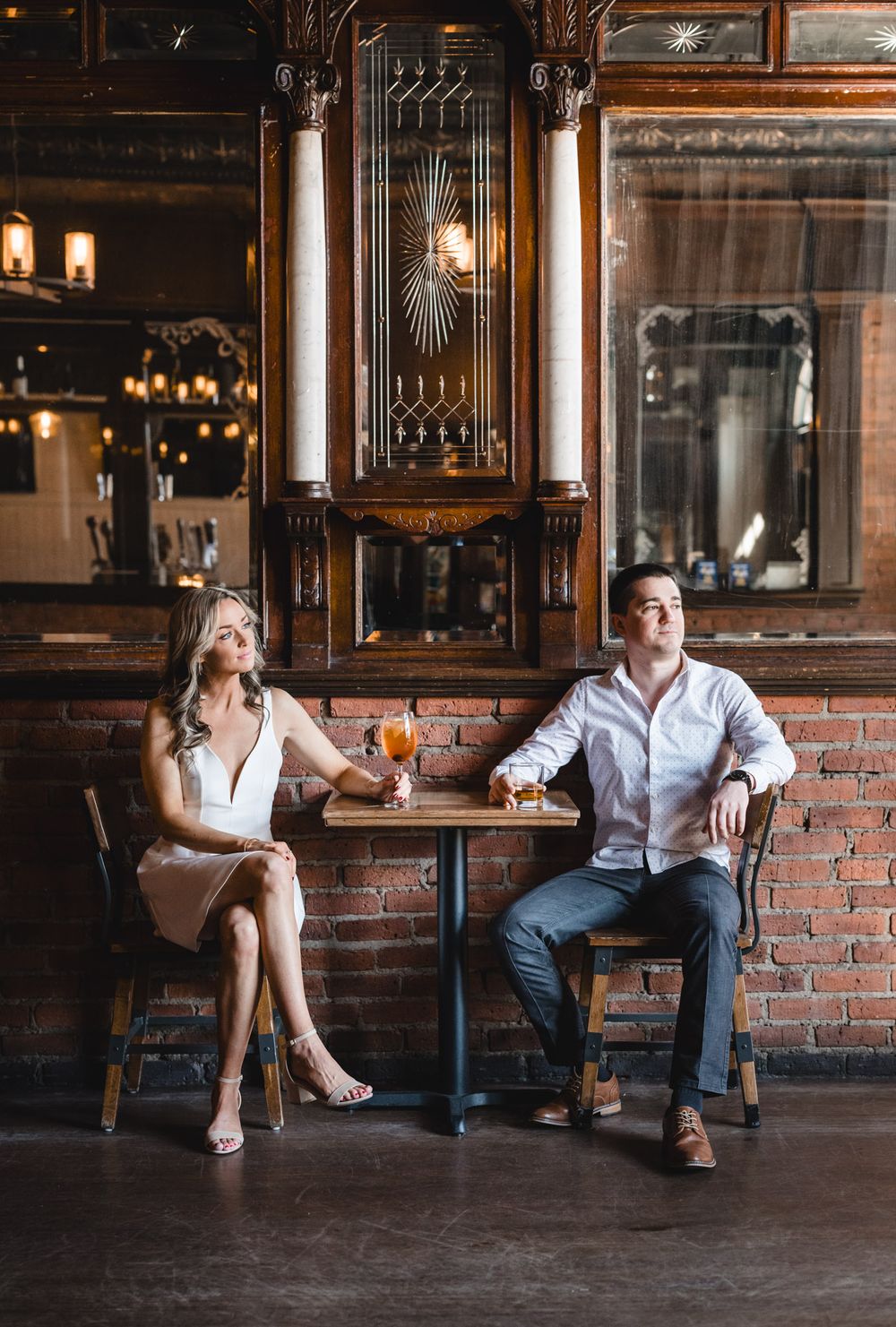 Couple enjoying drinks at an elegant bar with vintage woodwork and exposed brick walls.