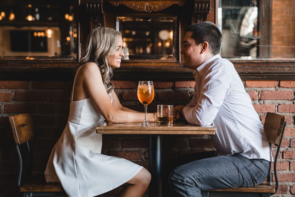 Two people engaged in conversation at a cozy bar table with cocktails.