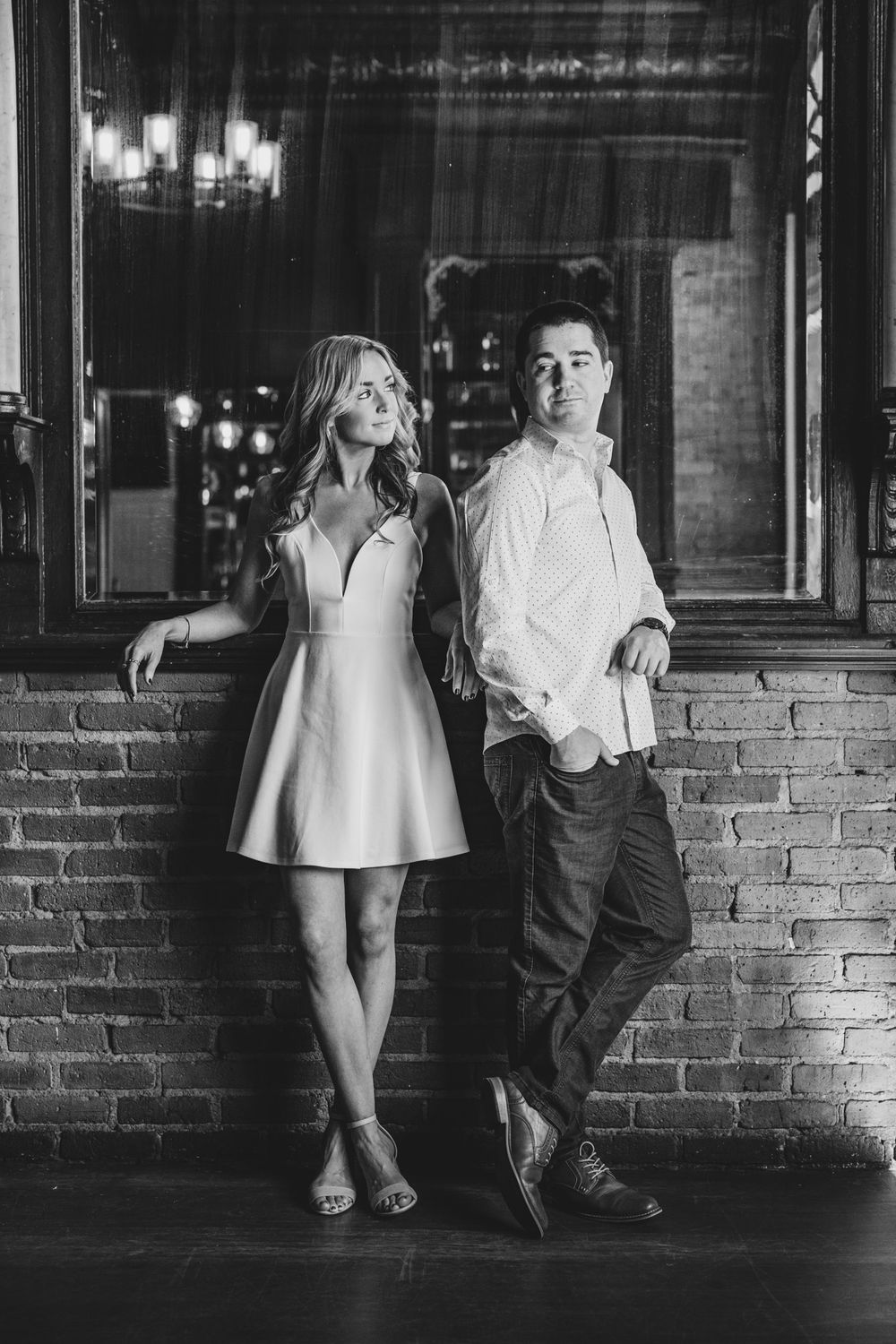 Black and white portrait of couple posing against brick wall in vintage bar setting.