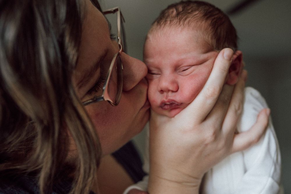 A tender moment captured as a parent gives their sleeping newborn baby a gentle kiss on the cheek. In home newborn session in hampton roads
