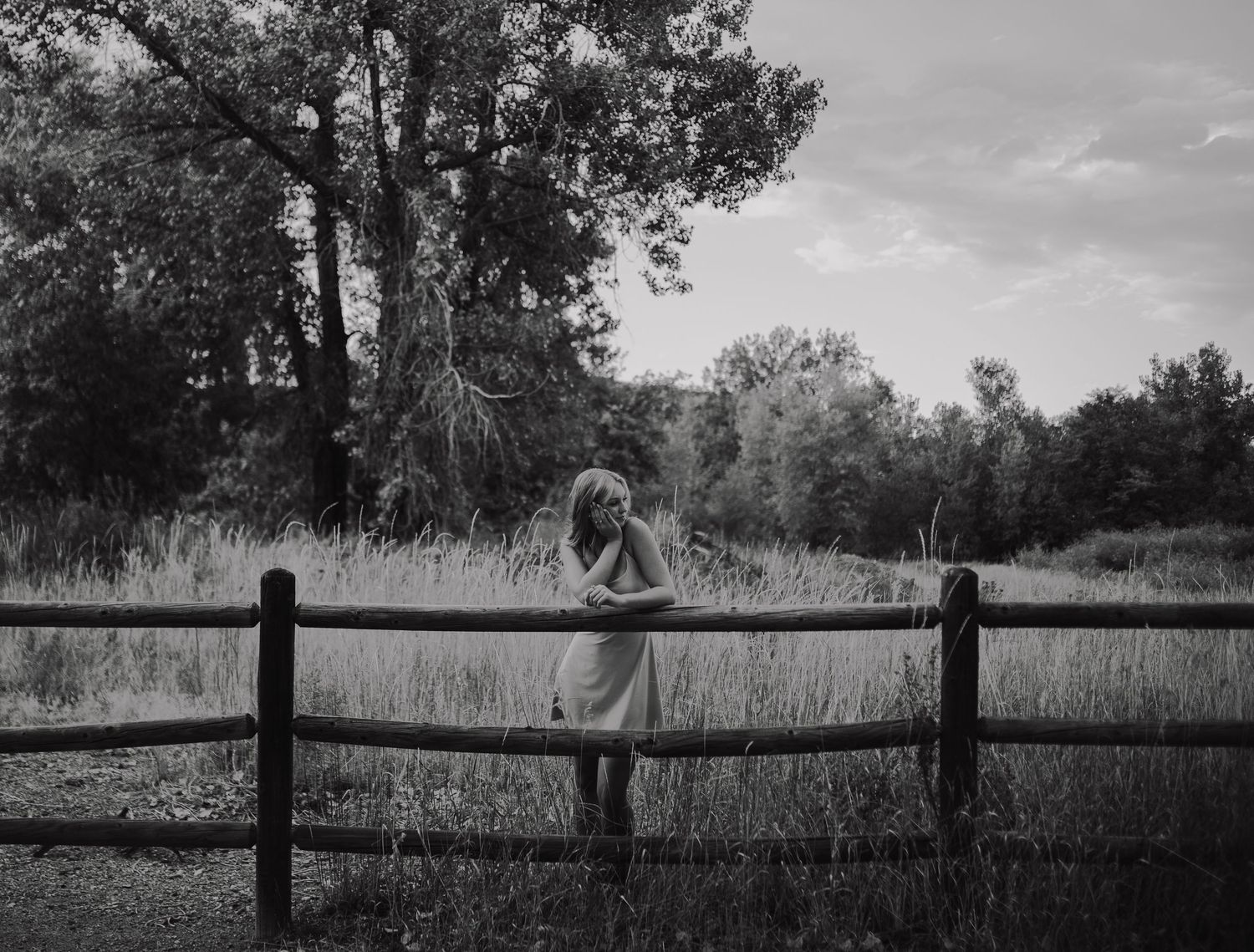 Black and white portrait of someone leaning on a rustic wooden fence in a serene countryside setting in Golden, Colorado