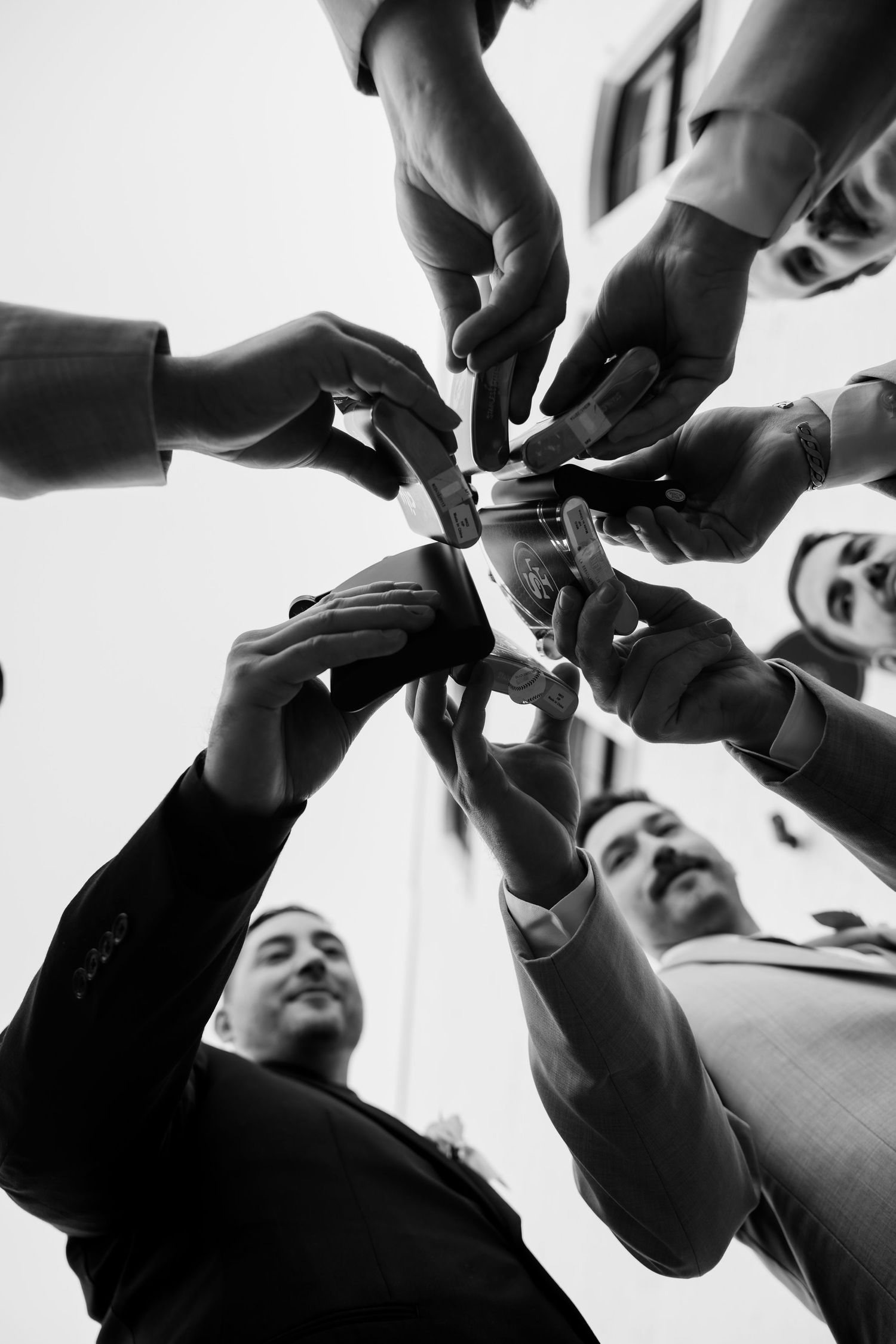 Multiple hands reach up to take photos or videos with mobile phones in a dramatic black and white composition.