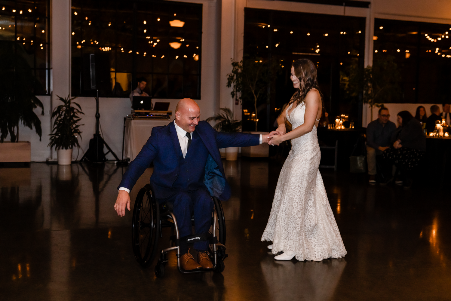 A couple shares their first dance at an elegant wedding reception in a dimly lit venue with decorative lighting.