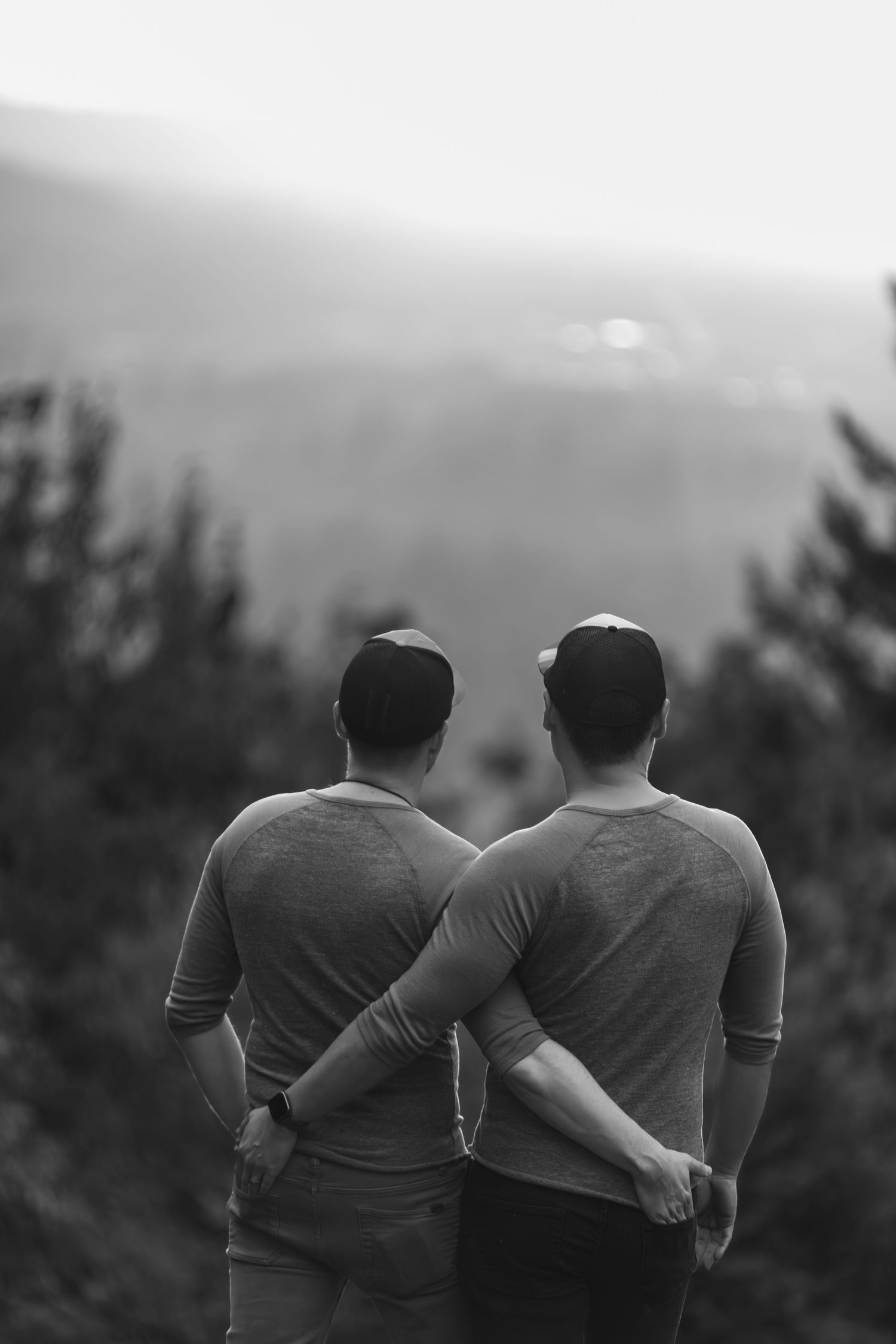 Two people walk together with arms around each other's backs on a scenic mountain trail at sunset.