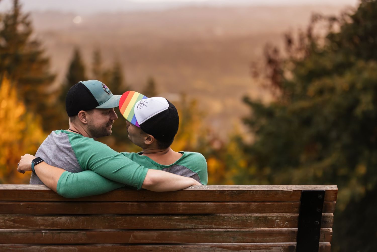 Two people share a romantic moment on a wooden bench overlooking an autumn landscape at sunset.