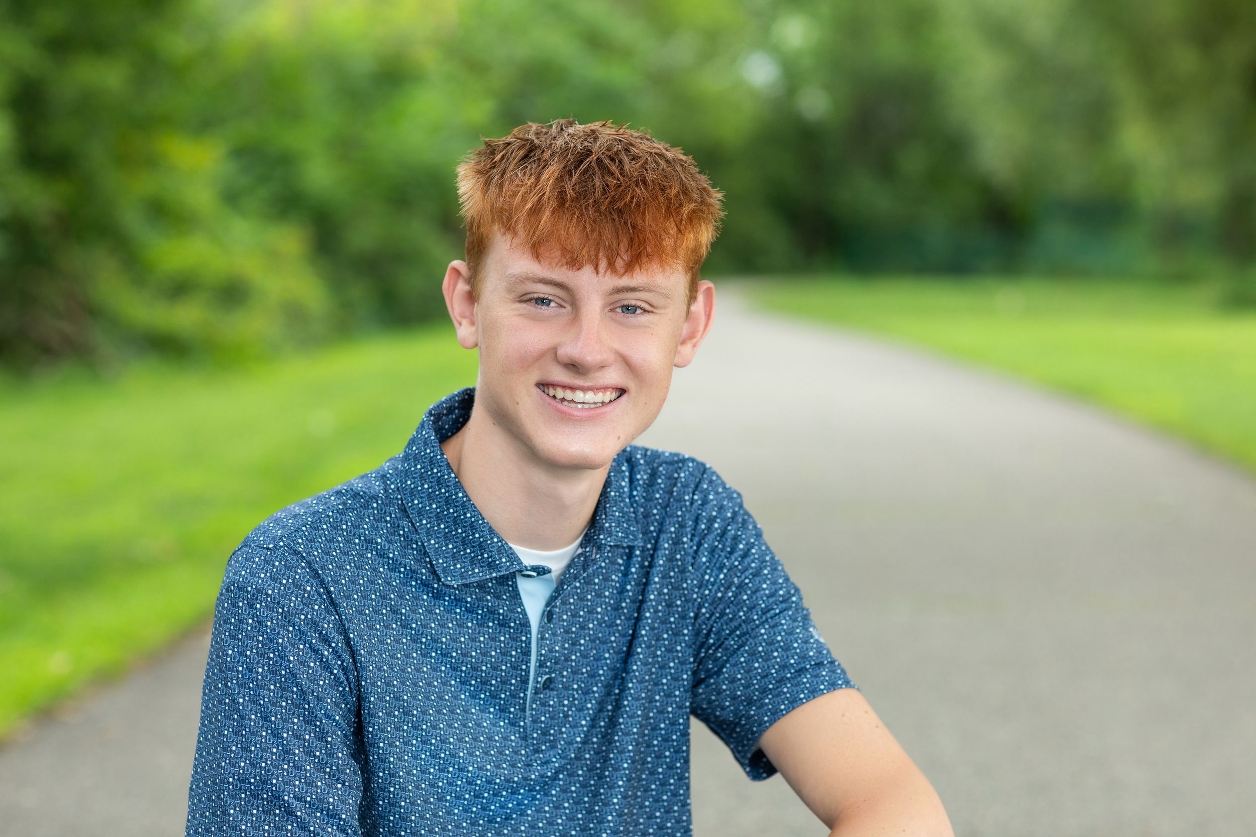 Young person in casual attire sitting outdoors against lush green natural background.