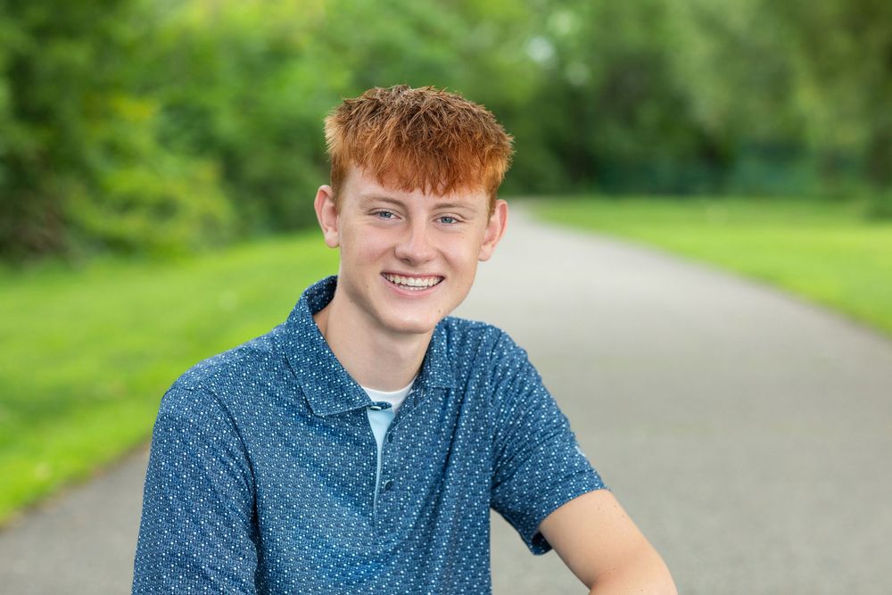 Young person in casual attire sitting outdoors against lush green natural background.
