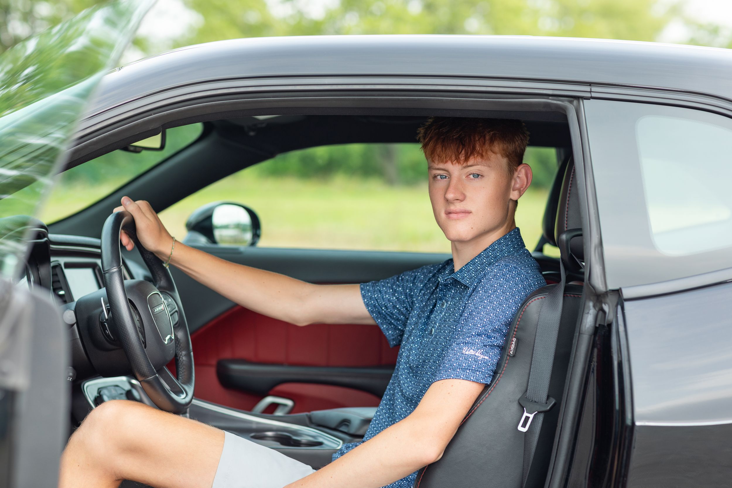 Person sitting in driver's seat of modern car with red interior details.