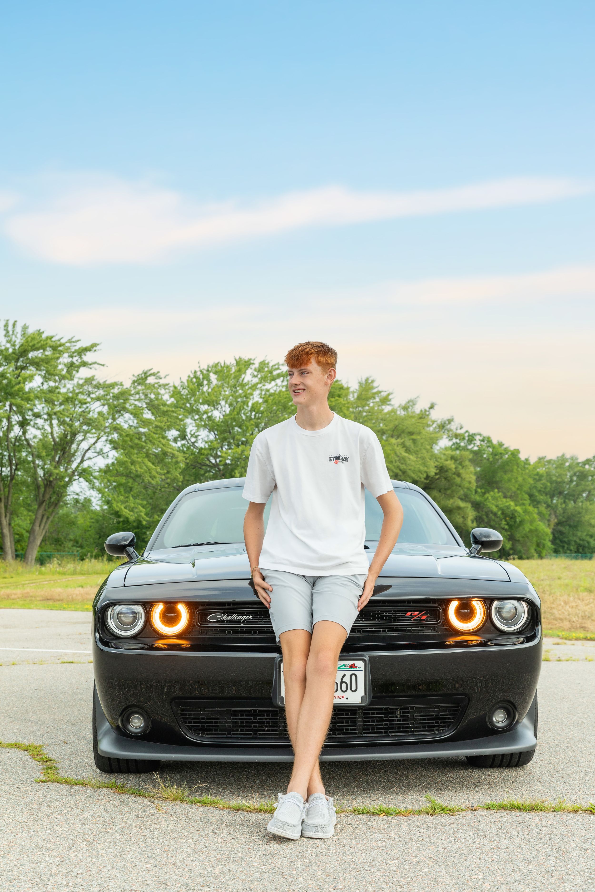 A black Dodge Challenger with glowing orange halo headlights parked on a rural road at dusk.