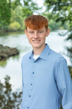 Portrait of someone wearing a light blue checkered dress shirt outdoors with trees and water in the background.