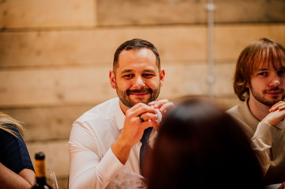 Wedding guests laugh and smile during a joyful reception celebration at an indoor venue.