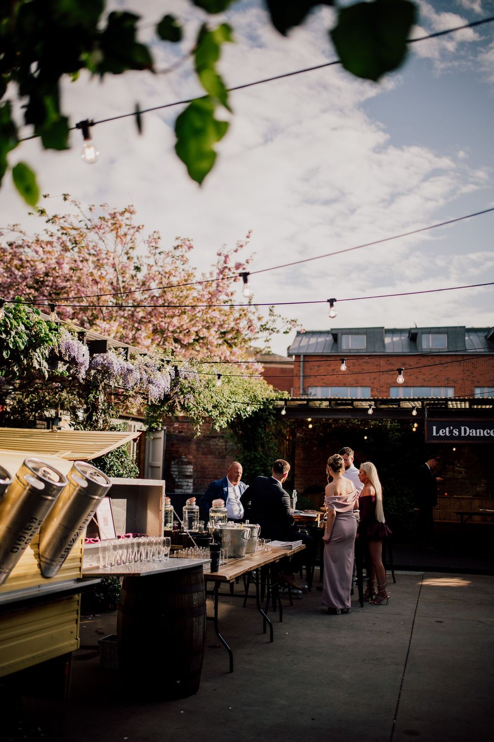 Outdoor rooftop venue decorated with string lights and cherry blossoms during a wedding reception at sunset.