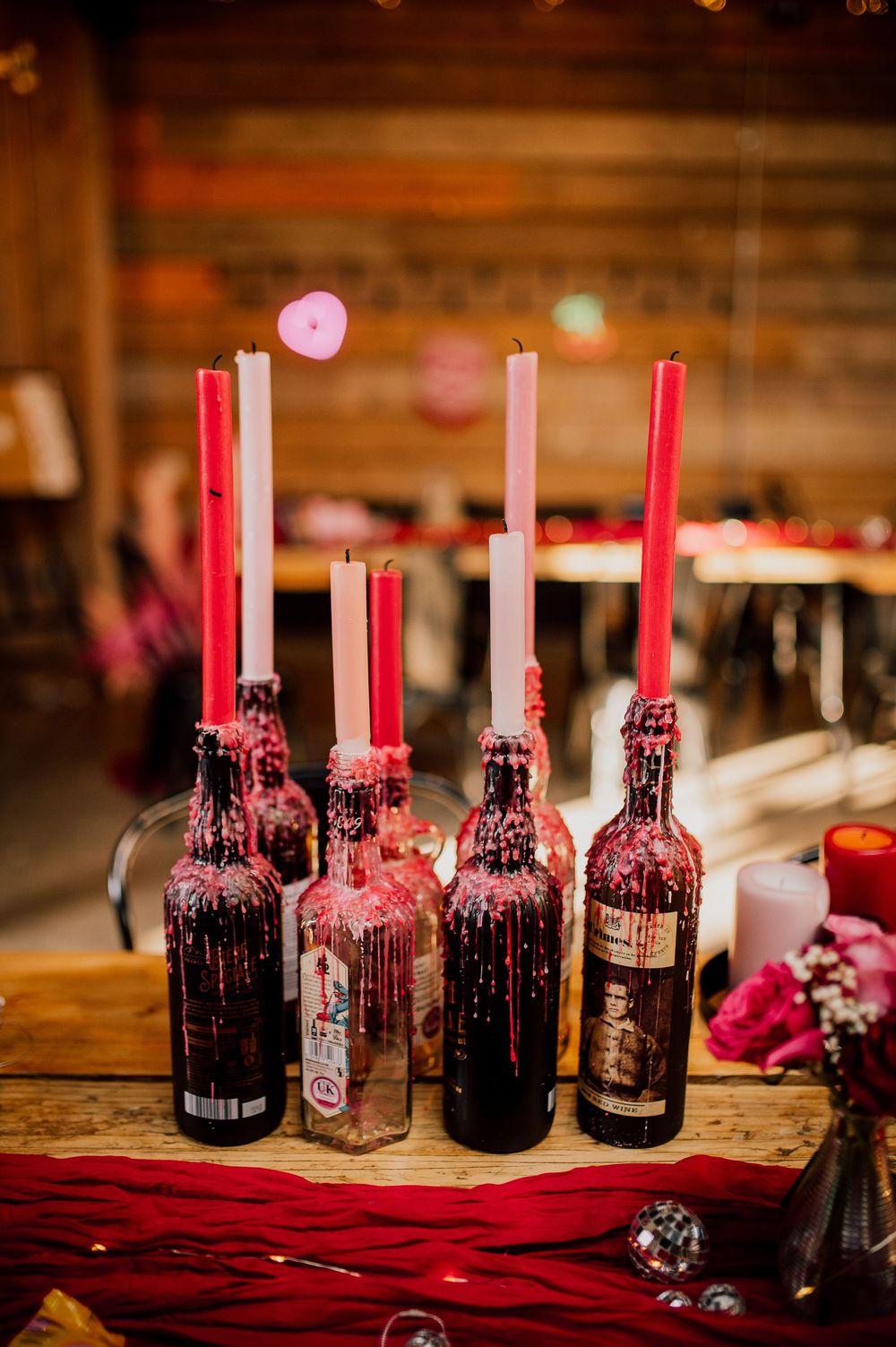 Glass bottles decorated with pink candles arranged on a rustic wooden surface create an elegant wedding table centerpiece.
