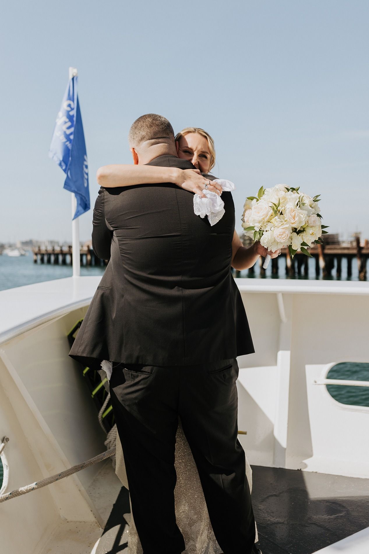 Two people in formal attire embrace emotionally during an outdoor wedding ceremony on a boat in San Diego.