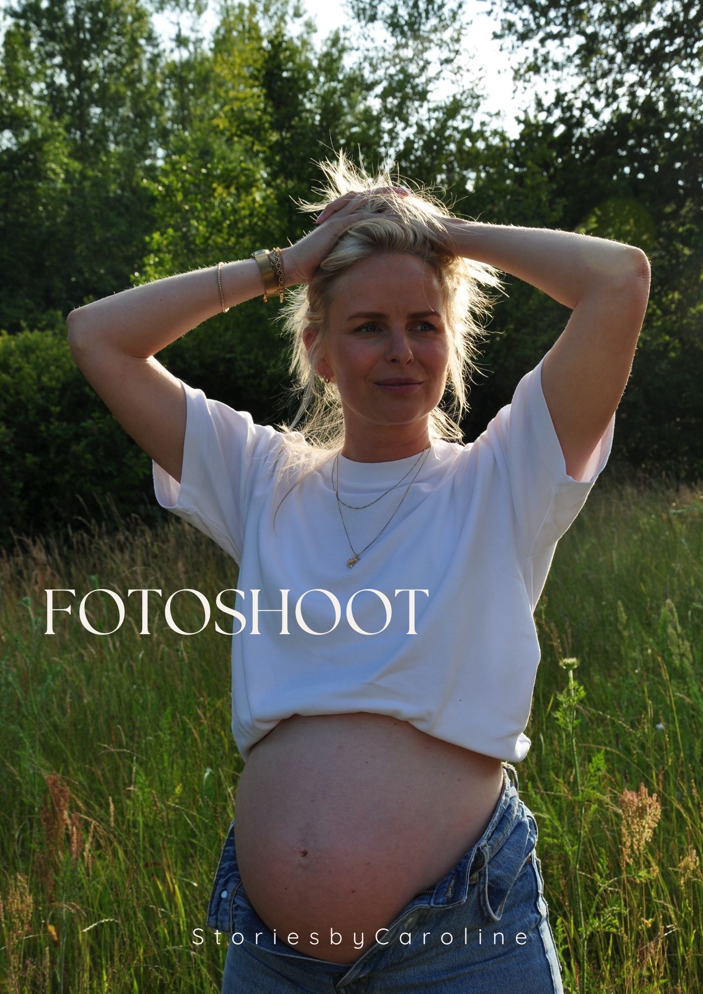 Pregnant woman in white t-shirt and jeans posing in a green field during a maternity fotoshoot.