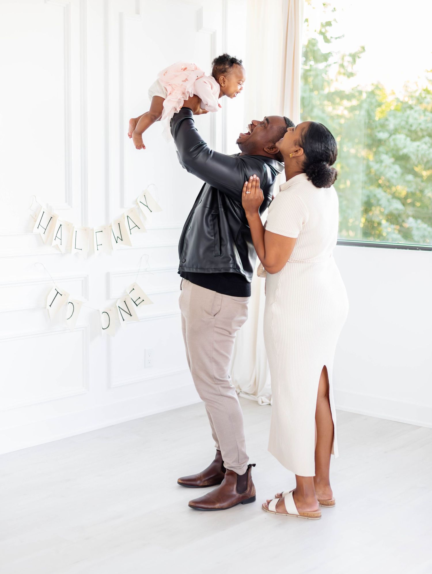 A couple shares a romantic dance in an elegant white room with natural light streaming through windows.