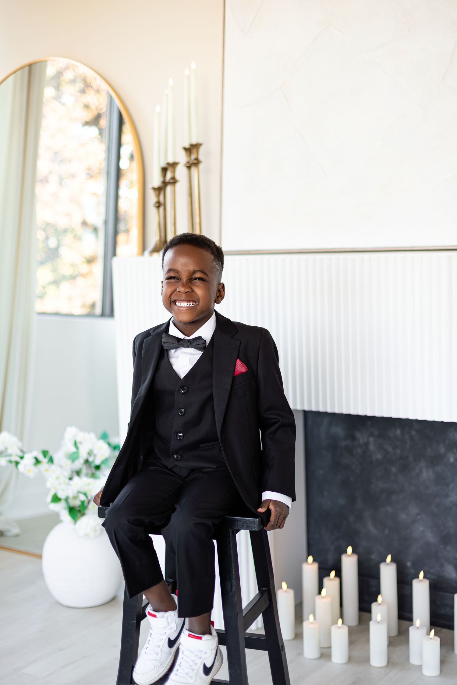 A joyful person in a black tuxedo sits and laughs while surrounded by white candles in an elegant setting.