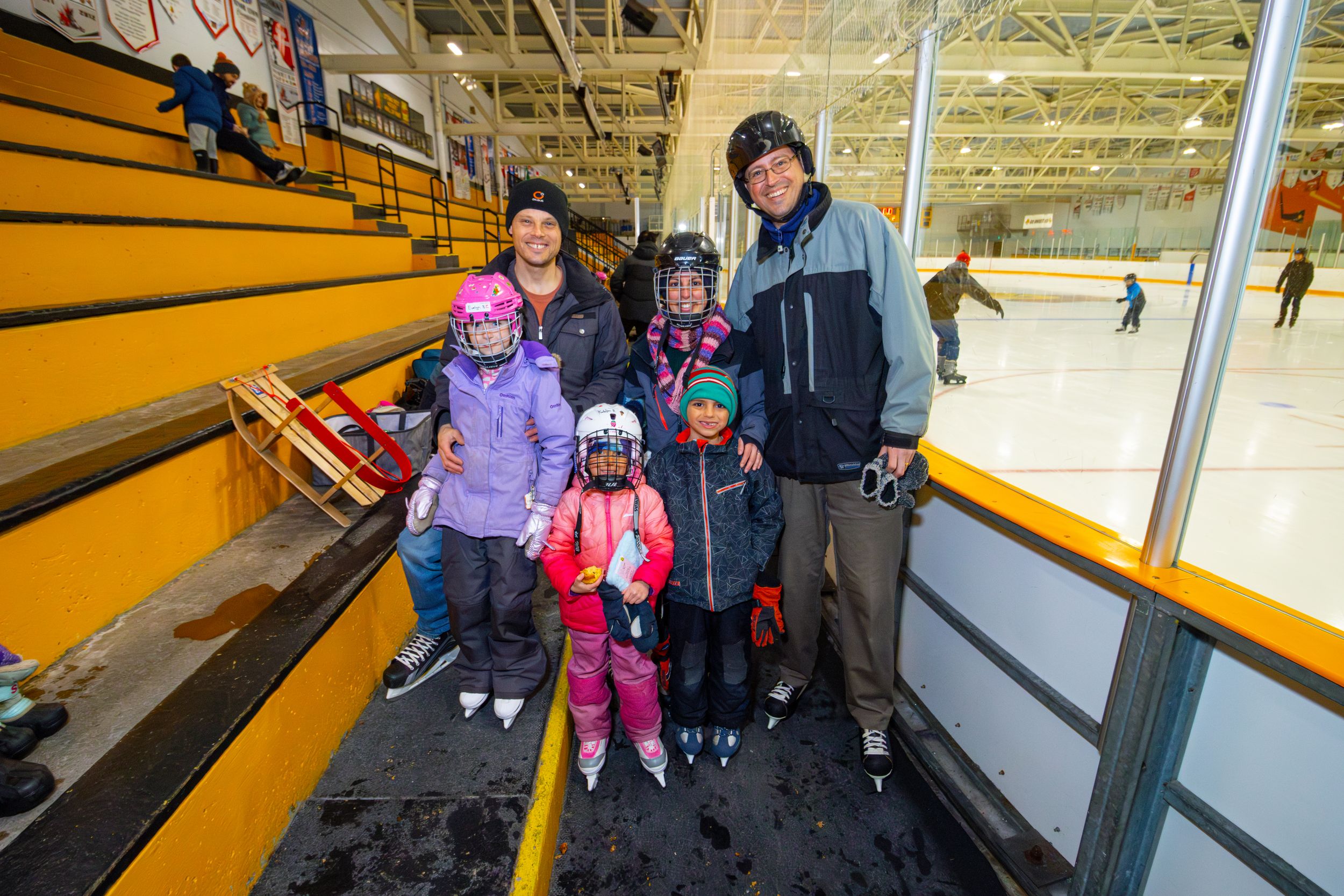 Group of skaters practicing at an indoor ice rink with yellow barriers along the edges.