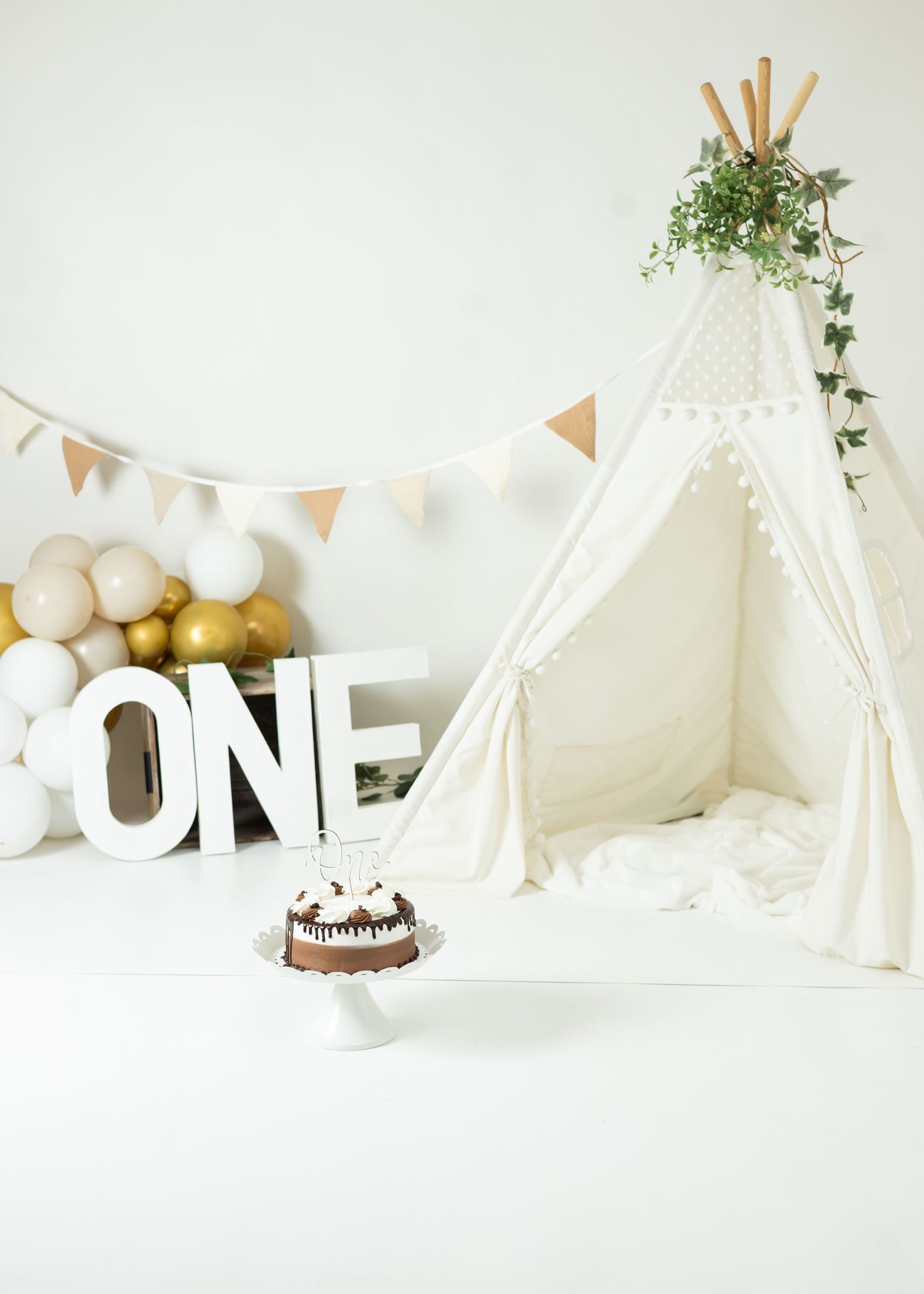 White and gold teepee tent party setup with ONE letter decorations and balloons for a first birthday celebration.