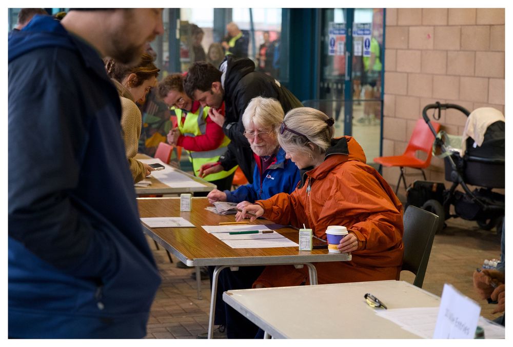 Volunteers in high-visibility vests assist runners at registration tables during an organized running event.
