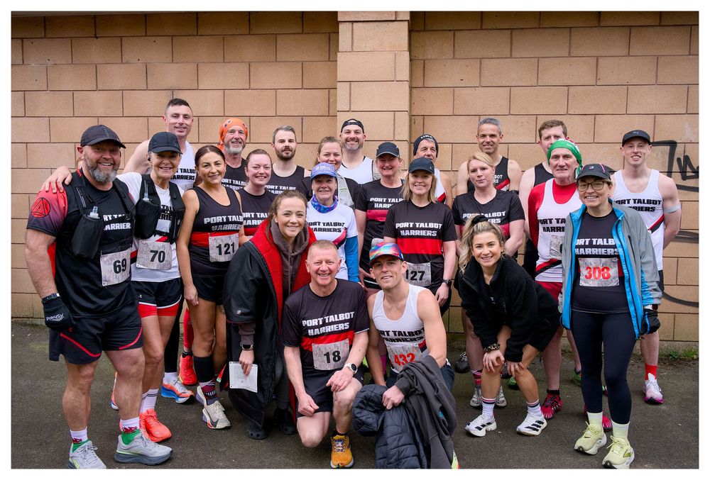 Large group of runners in matching black and red race shirts posing together before a charity fun run event.
