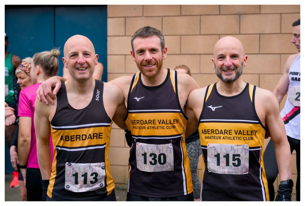Three male runners wearing Aberdare Valley Athletic Club vests with race numbers 113, 130, and 115 pose together smiling.