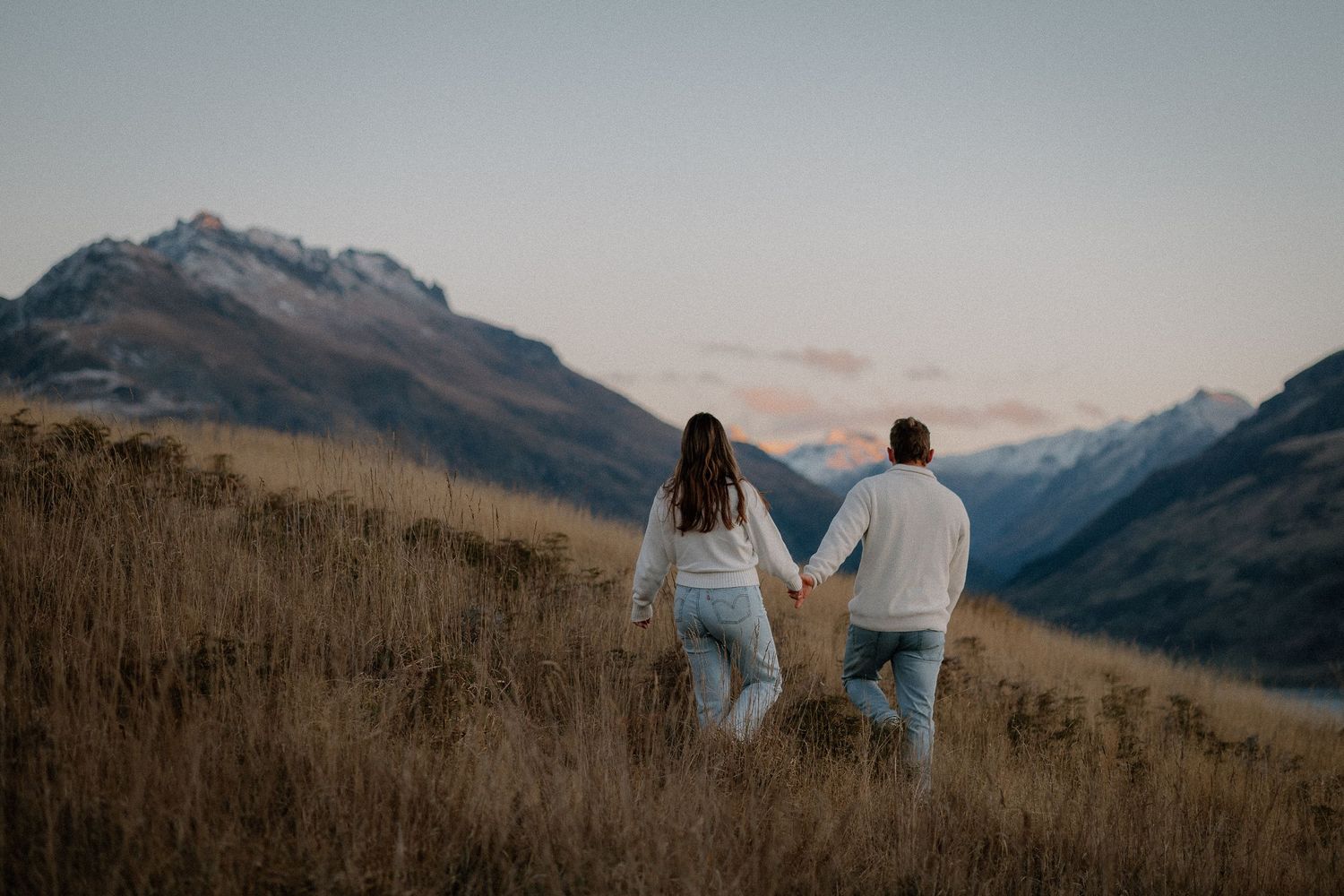 A couple shares an intimate moment in a golden wheat field against a bright blue sky during sunset.