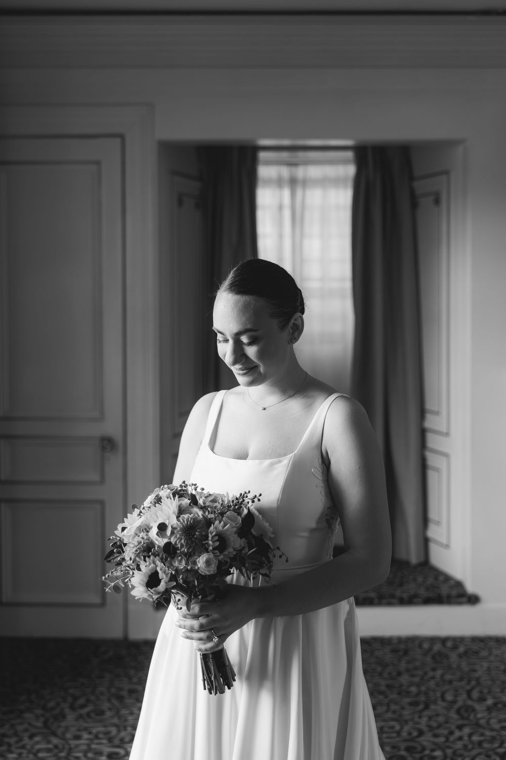 A person in a white dress holds a delicate bouquet of flowers while standing in a sunlit room.