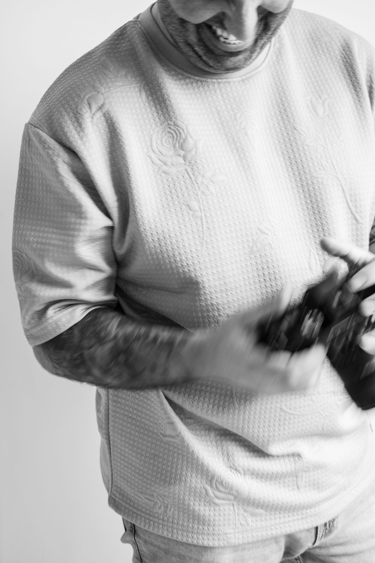 Person in white textured sweater holds camera in black and white portrait.