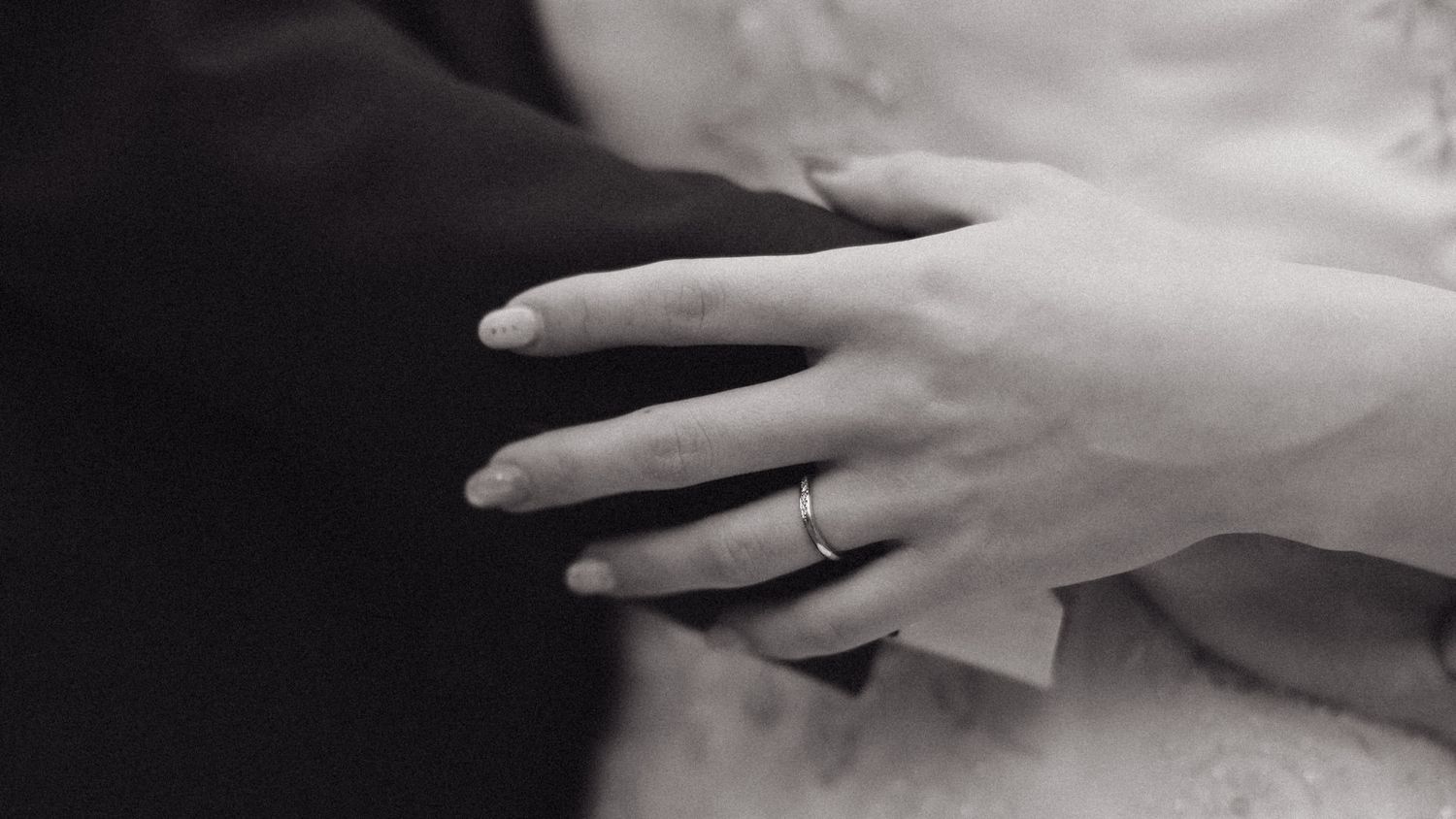 A close-up black and white photograph shows hands wearing wedding rings against a light fabric background. Couple photoshoot Sagrada Familia
