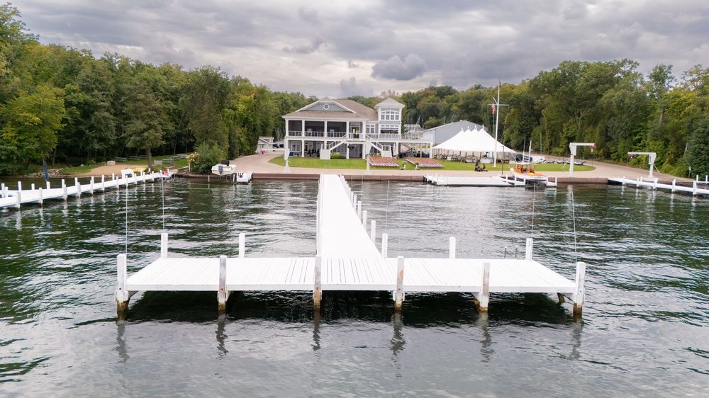 Aerial view of a white dock extending into a lake with a waterfront wedding venue surrounded by lush trees.