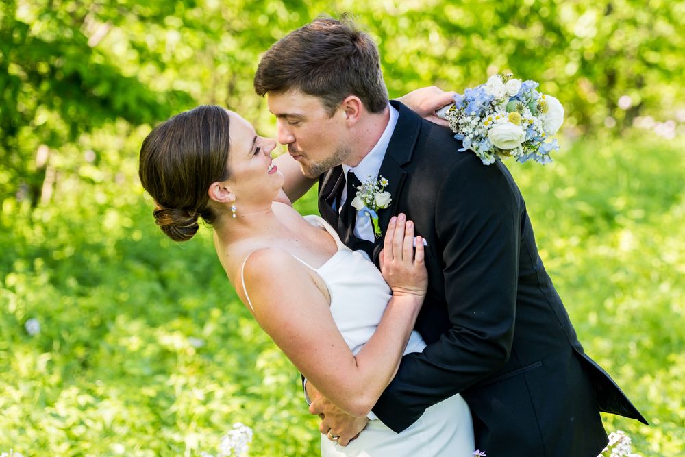 Bride and groom sharing romantic kiss outdoors surrounded by lush green foliage.