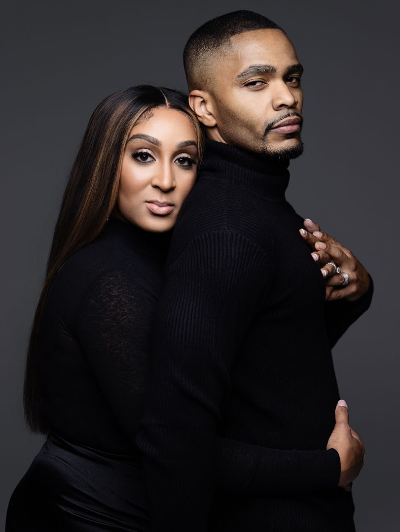 Elegant couple in matching black turtlenecks posing together against a dark gray studio background.
