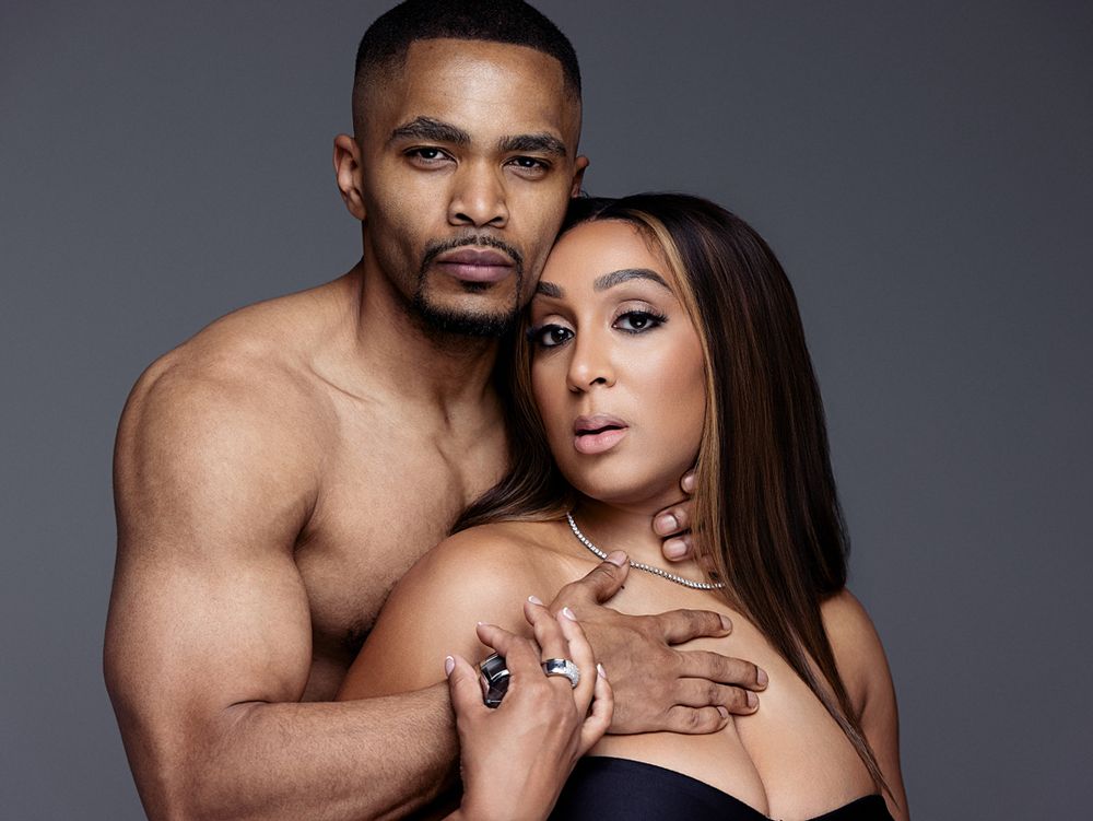 A muscular shirtless man embraces a woman in a strapless top in a professional studio portrait shoot.