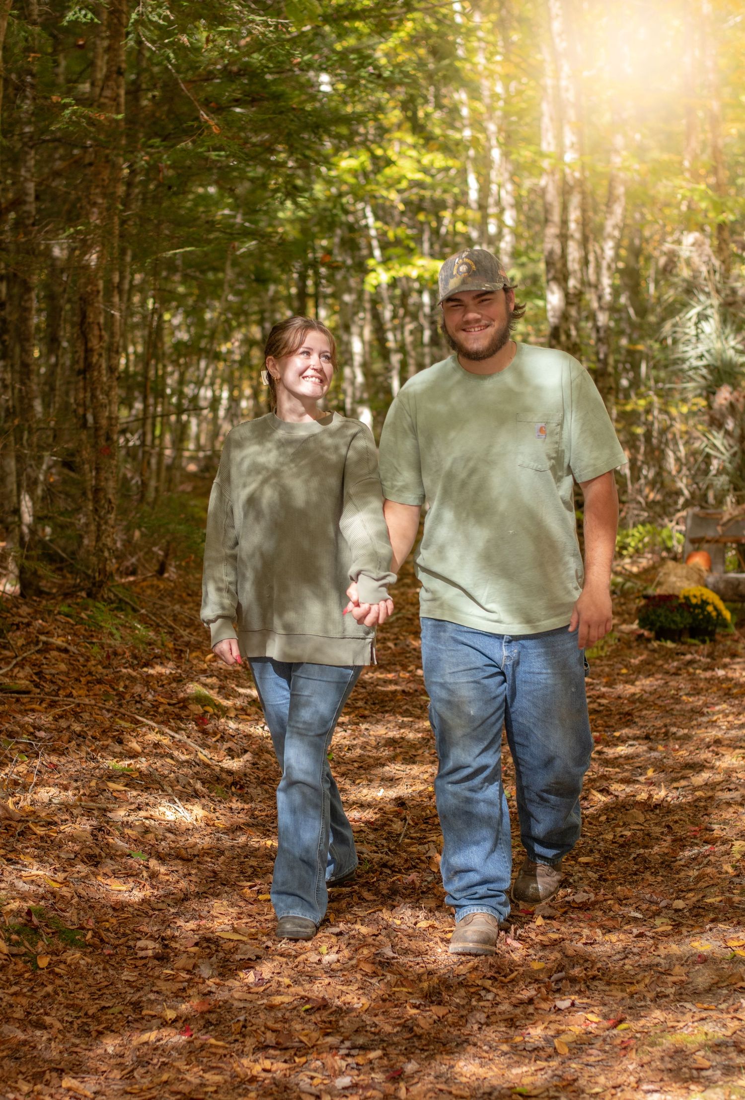 Couple walking hand in hand on a sunlit forest trail wearing casual attire.