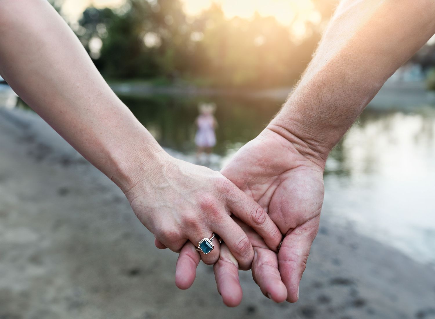 A series of hands holding each other against a blurred sunset background over water.