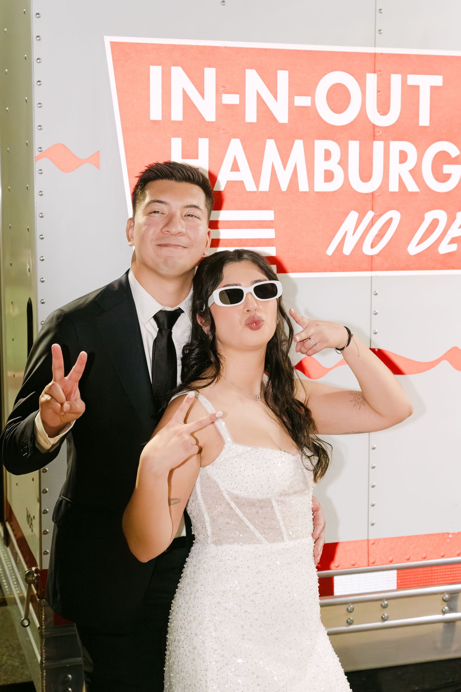 A couple poses playfully in front of an In-N-Out Burger truck at what appears to be a wedding celebration.