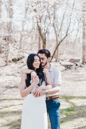 A couple embraces tenderly in a sunlit forest setting during their engagement photo session.