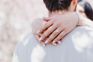 Close-up view of hands holding each other tenderly against a soft white background.