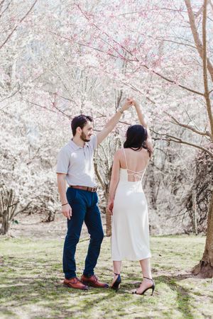 Romantic couple poses together under blooming cherry blossom trees in a spring garden setting.