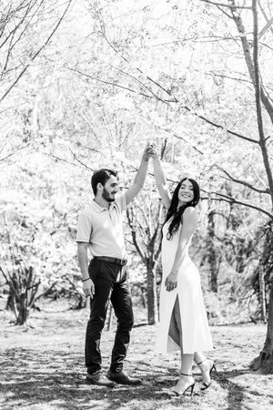 Candid black and white photos capture a couple sharing joyful moments beneath flowering trees in a park.