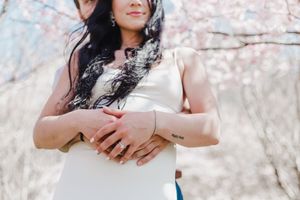 A couple holds hands while standing among blooming cherry blossom trees during a romantic spring photoshoot.