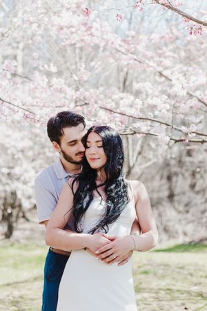 A romantic couple embraces under blooming cherry blossom trees during a spring photo session.